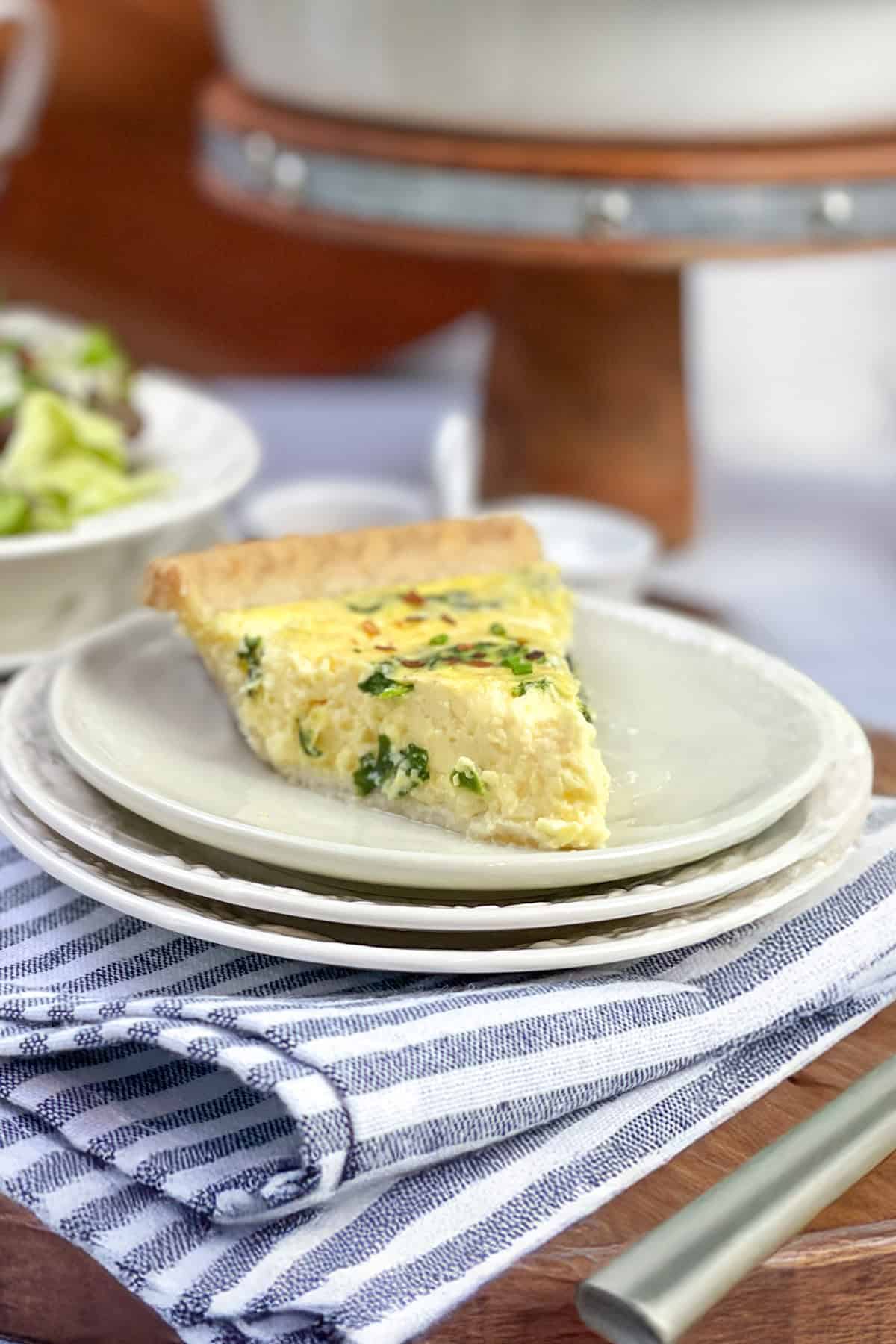 Slice of freshly baked spinach quiche on a plate with a green salad in the background, ready for serving.