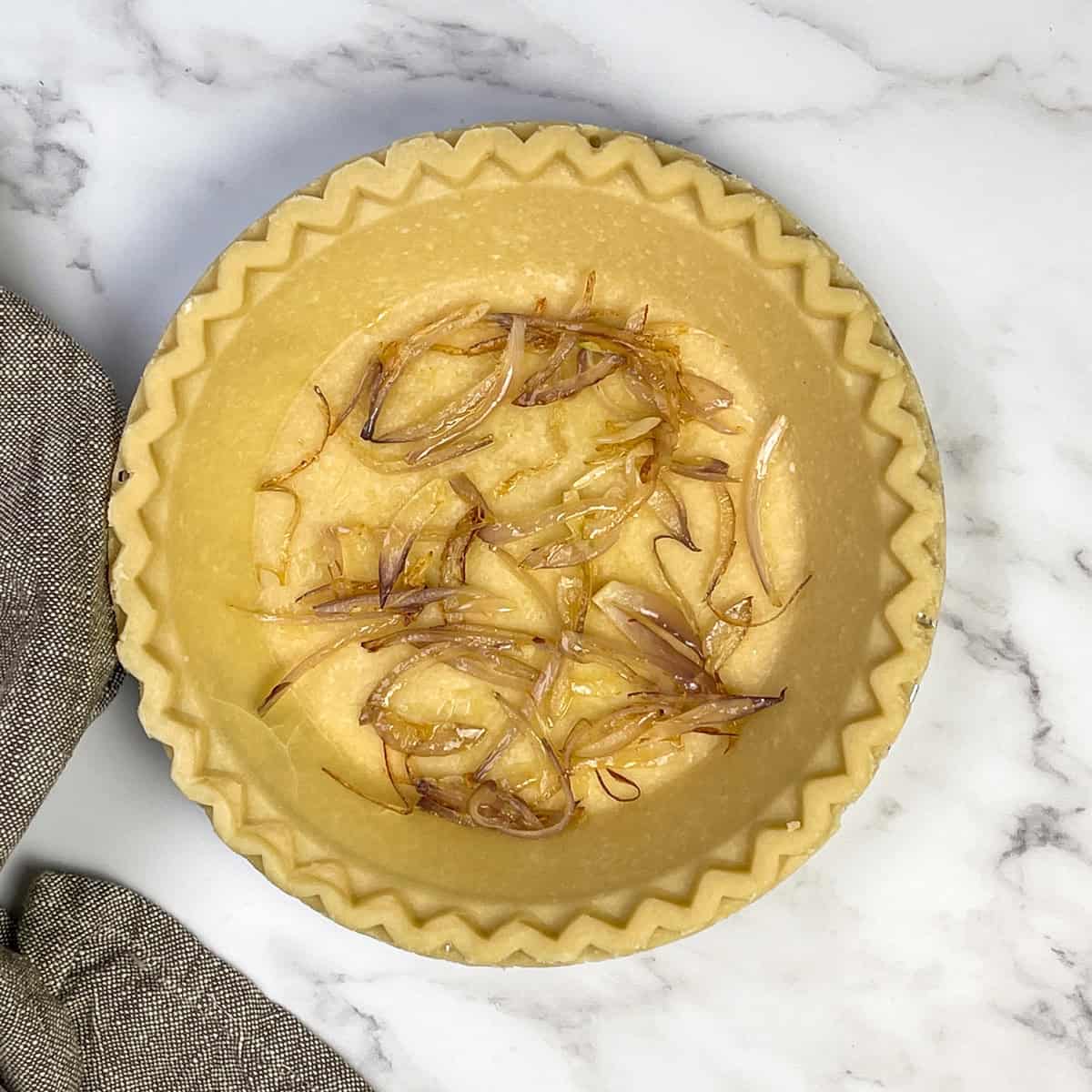 Sauteed shallots in the bottom of a frozen pie crust to be baked into a spinach quiche.