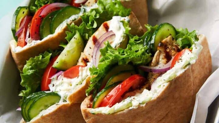 Three pita pockets filled with grilled chicken, lettuce, cucumber, tomato, red onion, and a creamy sauce—an ideal January DASH Diet Dinner—served on parchment paper in a metal tray.