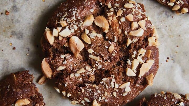 Four chocolate cookies topped with chopped nuts on parchment paper, with one cookie partially eaten—an unexpected sweet treat to complement your January Mediterranean Diet Dinners.