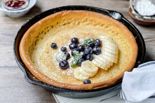 Banana Dutch Baby pancake in a cast iron skillet with sliced bananas and blueberries
