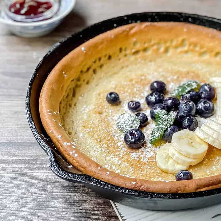 Banana Dutch Baby pancake in a cast iron skillet with sliced bananas and blueberries