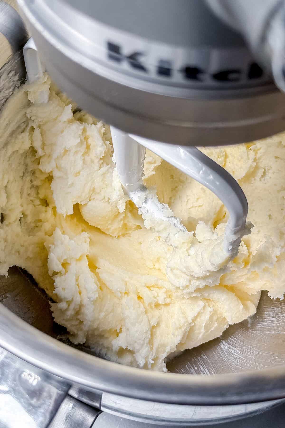 A stand mixer blends softened butter and sugar in a metal mixing bowl, creating a light, creamy mixture-the perfect base for an irresistible Almond Cake.