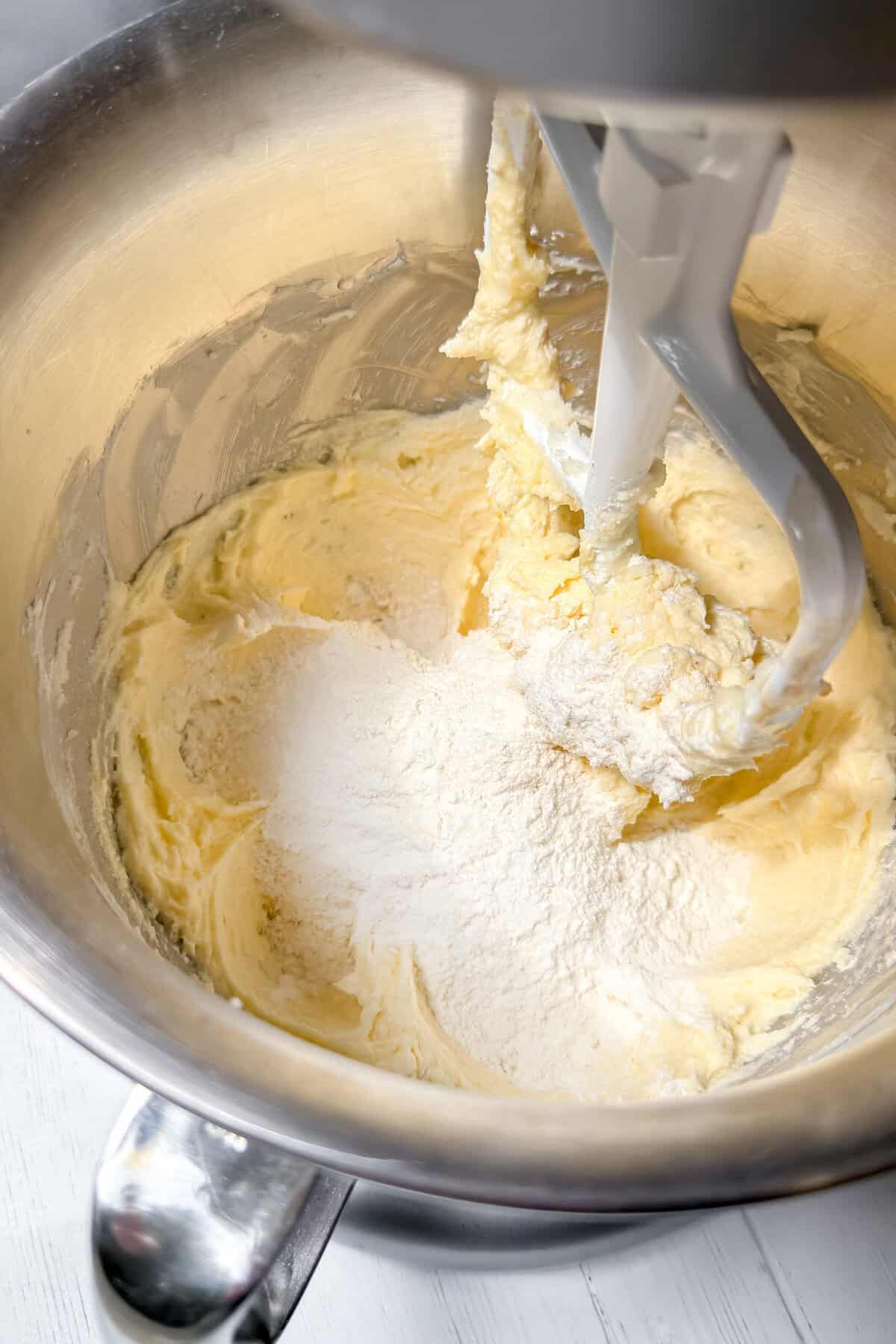 Electric mixer with paddle attachment blending flour into creamed butter and sugar in a stainless steel bowl for delicious Almond Cake.
