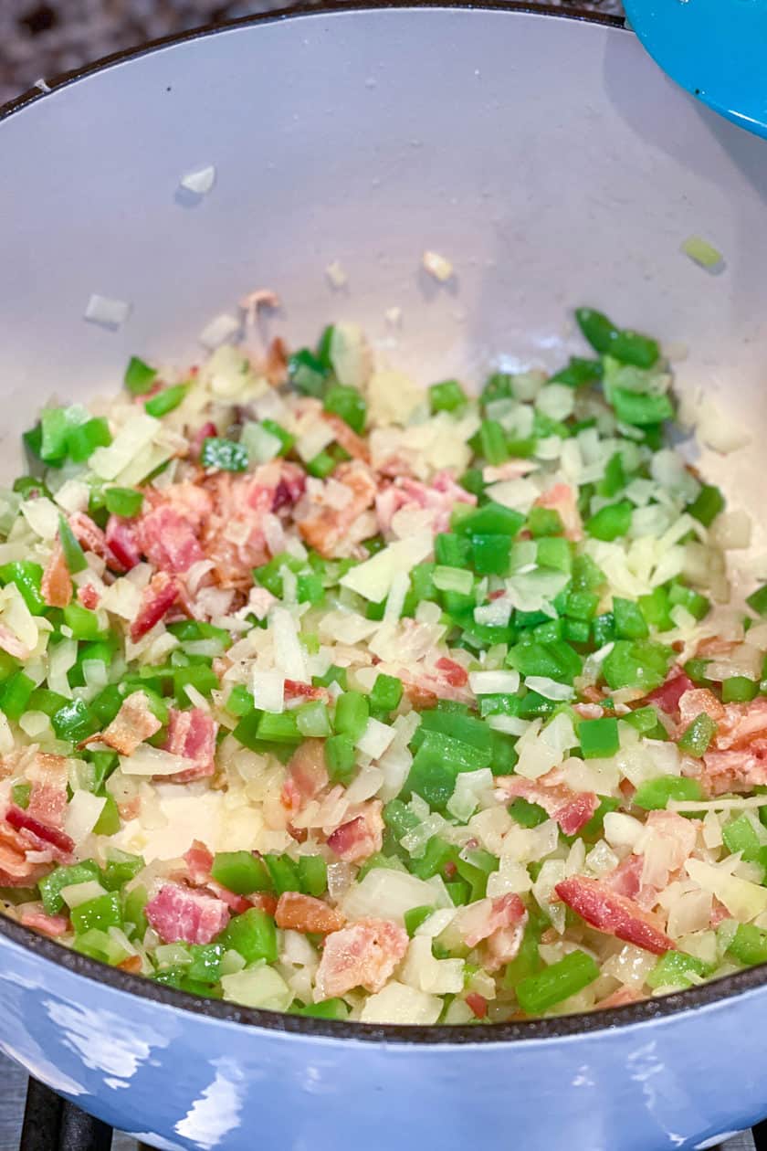 Top view of bacon, peppers, onions, and garlic sautéing in a pot