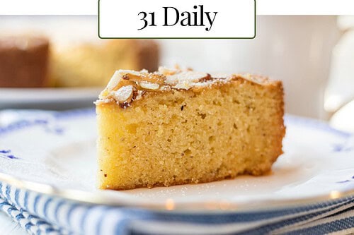 A round Almond Cake with sliced almonds on top, shown whole and as a single slice on a plate; includes text reading "Almond Cake, Elegantly simple. 31 Daily.