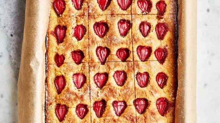 A rectangular baking tray lined with parchment paper holds a baked cake topped with rows of halved strawberries, cut into evenly sized squares—an irresistible treat inspired by Sheet Pan Mediterranean Diet Dinners.