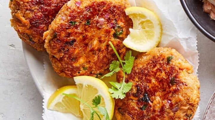 Three golden-brown fish cakes served on a white plate with lemon wedges and fresh cilantro garnish—perfect for March budget friendly dinners.