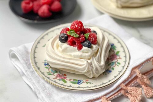 Heart Shaped Pavlova on a porcelain plate with fresh raspberries, blueberries, and mint leaves