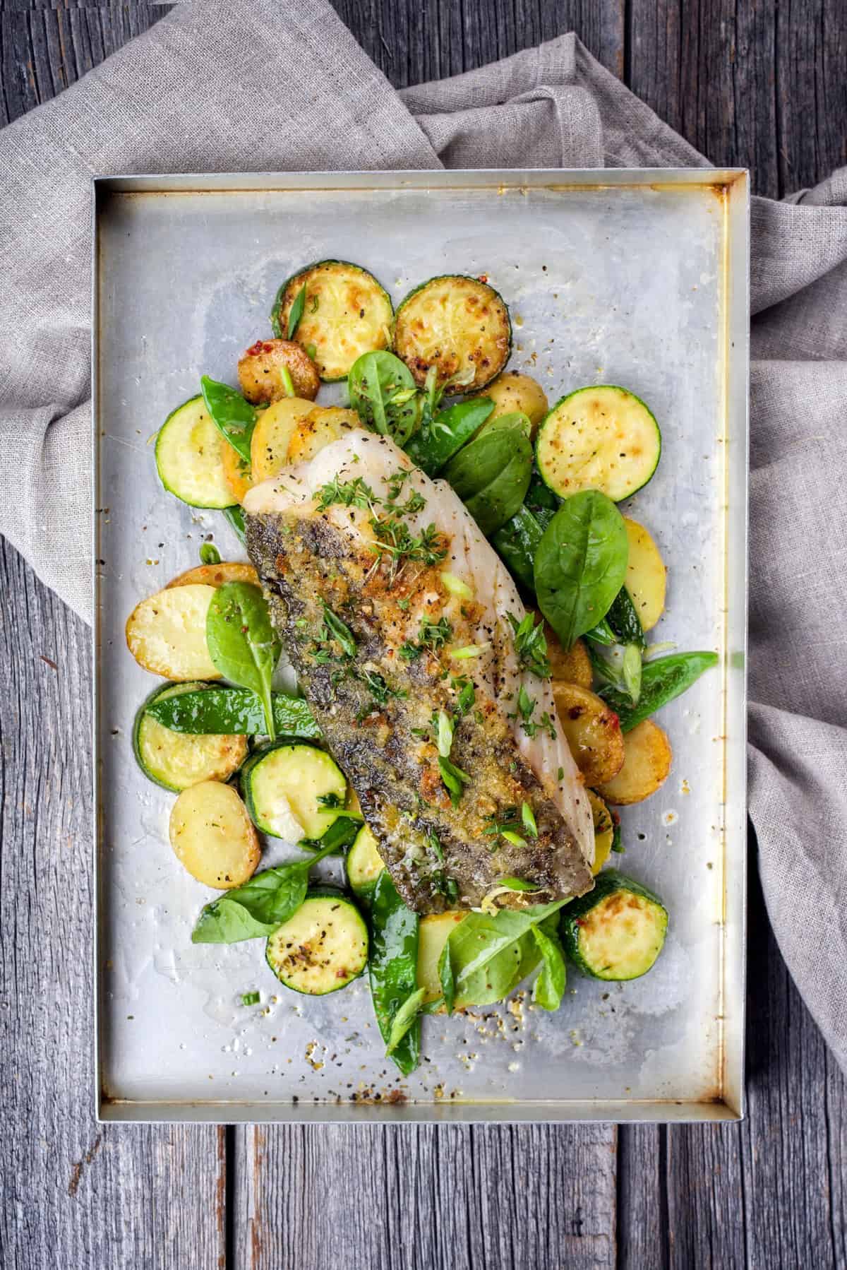 Baked Fish and Vegetables on a baking tray, sitting on a wooden surface, ready for serving.