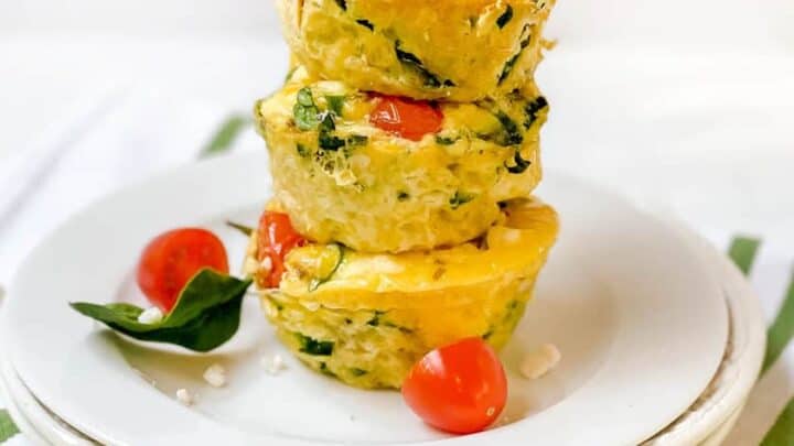 A glass filled with layers of yogurt, granola, and fresh blueberries, with a few blueberries scattered on the table around the glass.