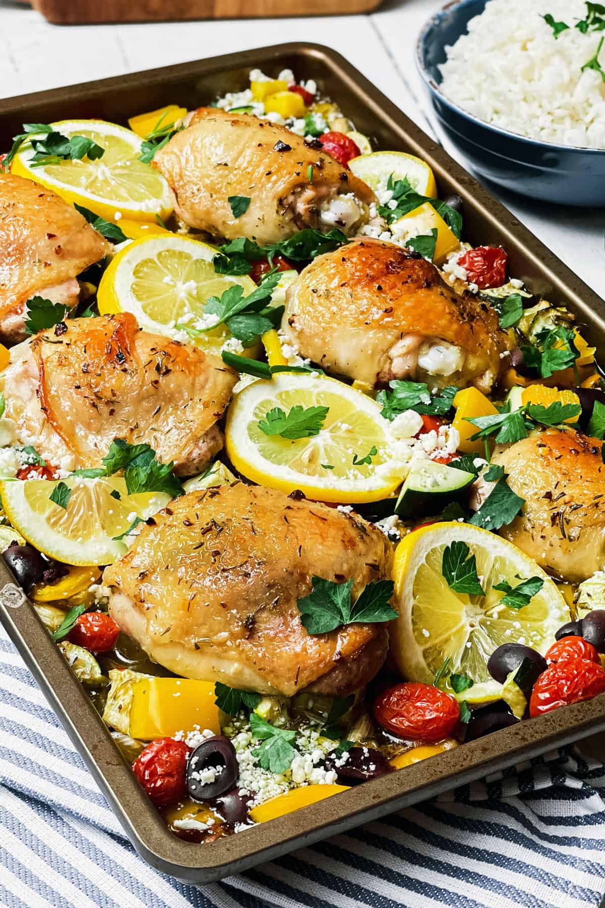 Baked Greek Chicken, lemons, veggies, and Kalamata olives on a sheet pan ready for serving.