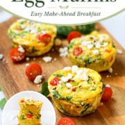 Four Mediterranean egg muffins with spinach, tomatoes, and feta on a wooden board, garnished with cherry tomatoes and crumbled cheese. These wholesome egg muffins make a perfect savory breakfast or snack.