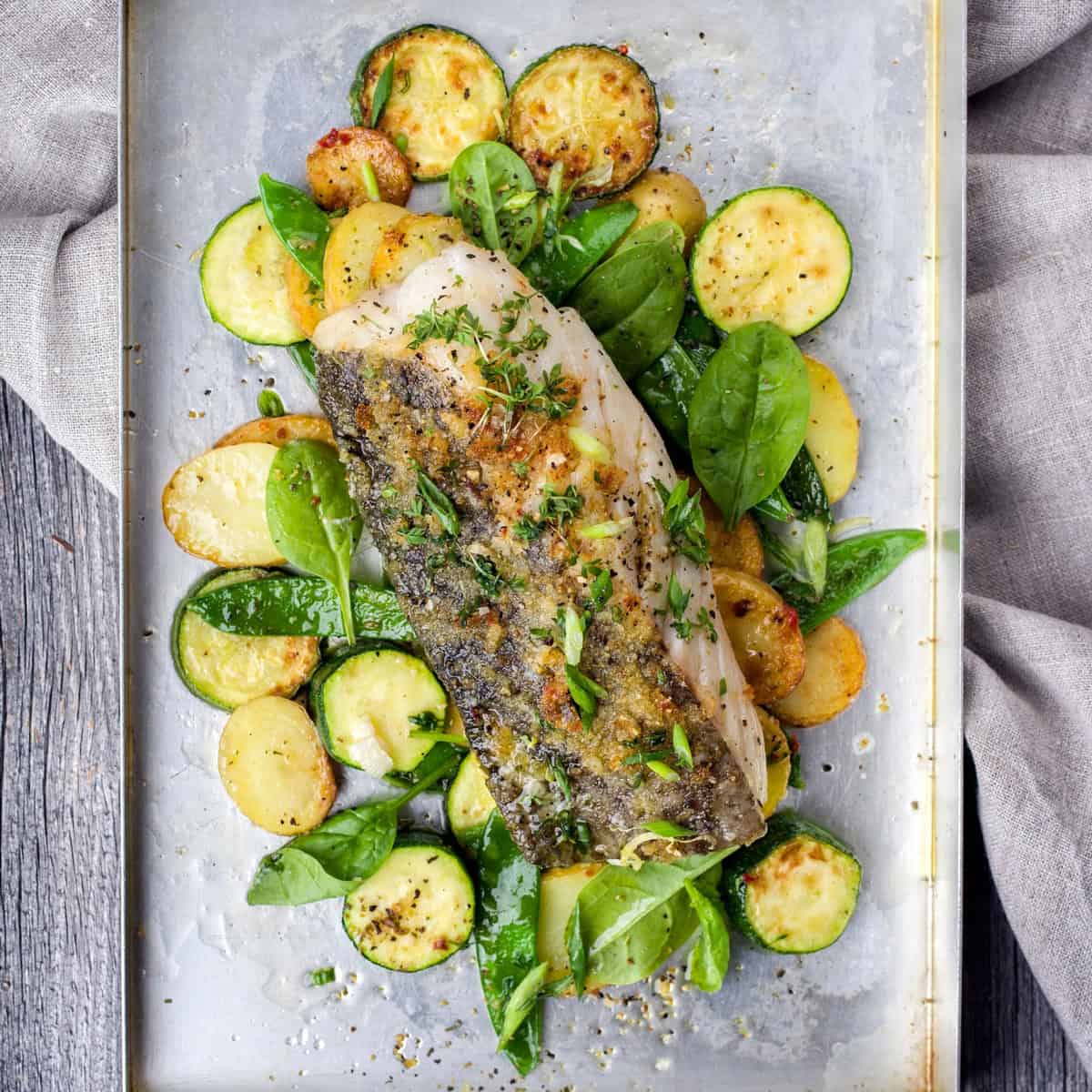 Baked Fish on a sheet pan with vegetables, fresh herbs, and salt and pepper ready for serving.