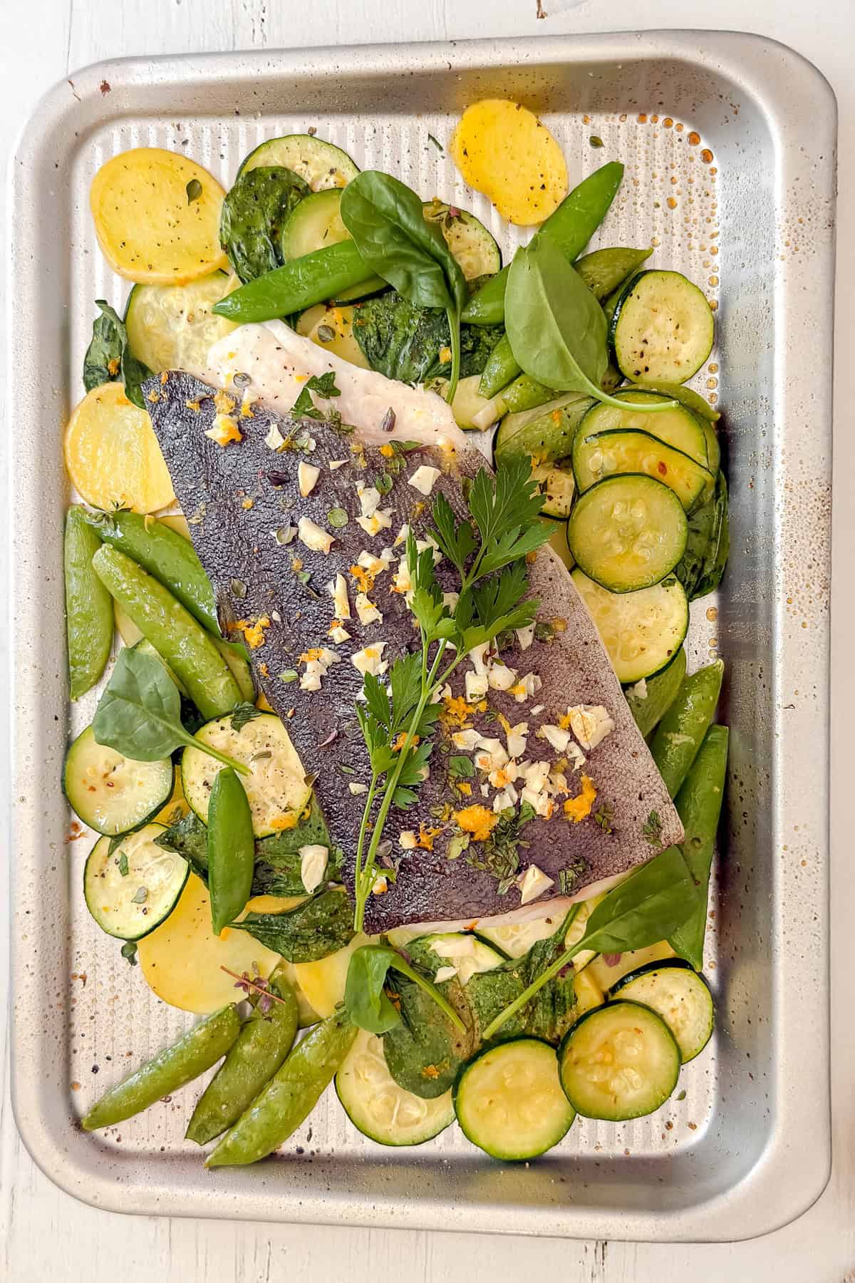 Just baked fish and vegetables, resting on a sheet pan and topped with fresh herbs for serving.