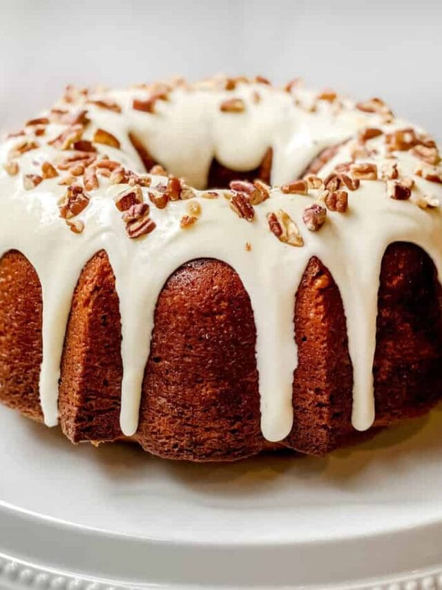 Unsliced Hummingbird Cake on a White Cake Stand with a Fresh Pineapple