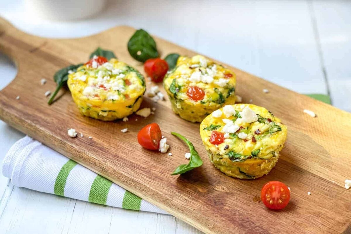 Mediterranean Egg Muffins on a wood board with chopped tomatoes and spinach
