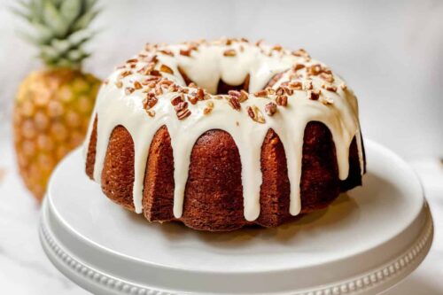 Unsliced Hummingbird Cake on a White Cake Stand with a Fresh Pineapple