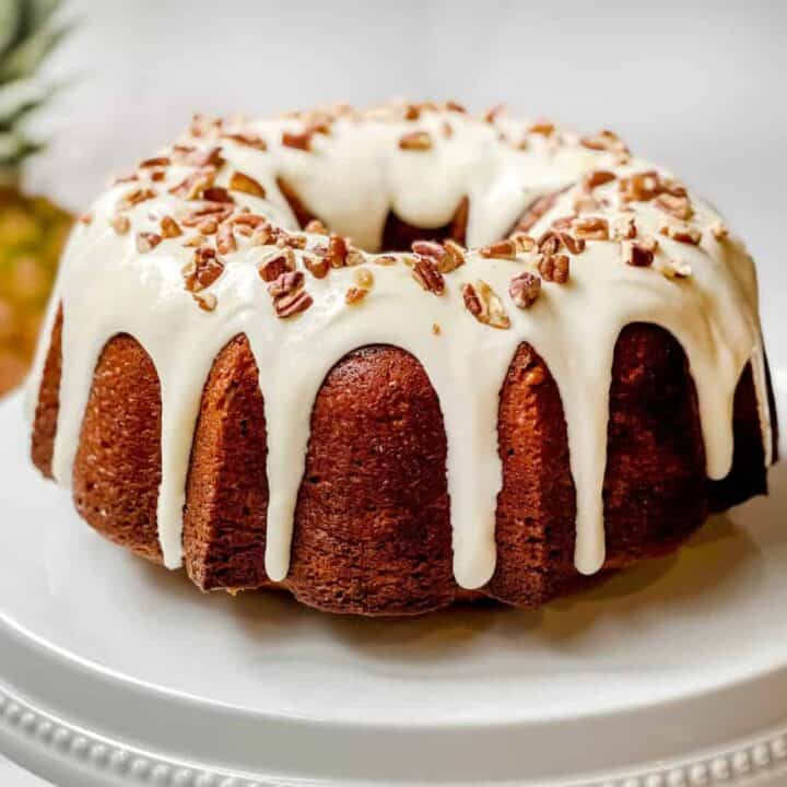 Unsliced Hummingbird Cake on a White Cake Stand with a Fresh Pineapple