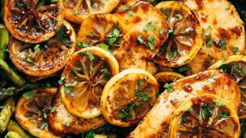 A skillet filled with cooked chicken breasts, asparagus, and lemon slices, garnished with chopped herbs—one of our Healthy 5 Ingredient Spring Dinners perfect for a quick, fresh meal.