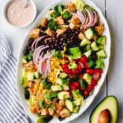 Oval platter with chopped lettuce, chicken, black beans, avocado, cherry tomatoes, corn, red onion, and cilantro-this chicken taco salad recipe is served with a creamy dressing on the side.
