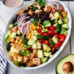 A chicken taco salad platter with diced chicken, avocado, cherry tomatoes, corn, black beans, red onion, lettuce, and cilantro, served with a creamy dressing on the side.