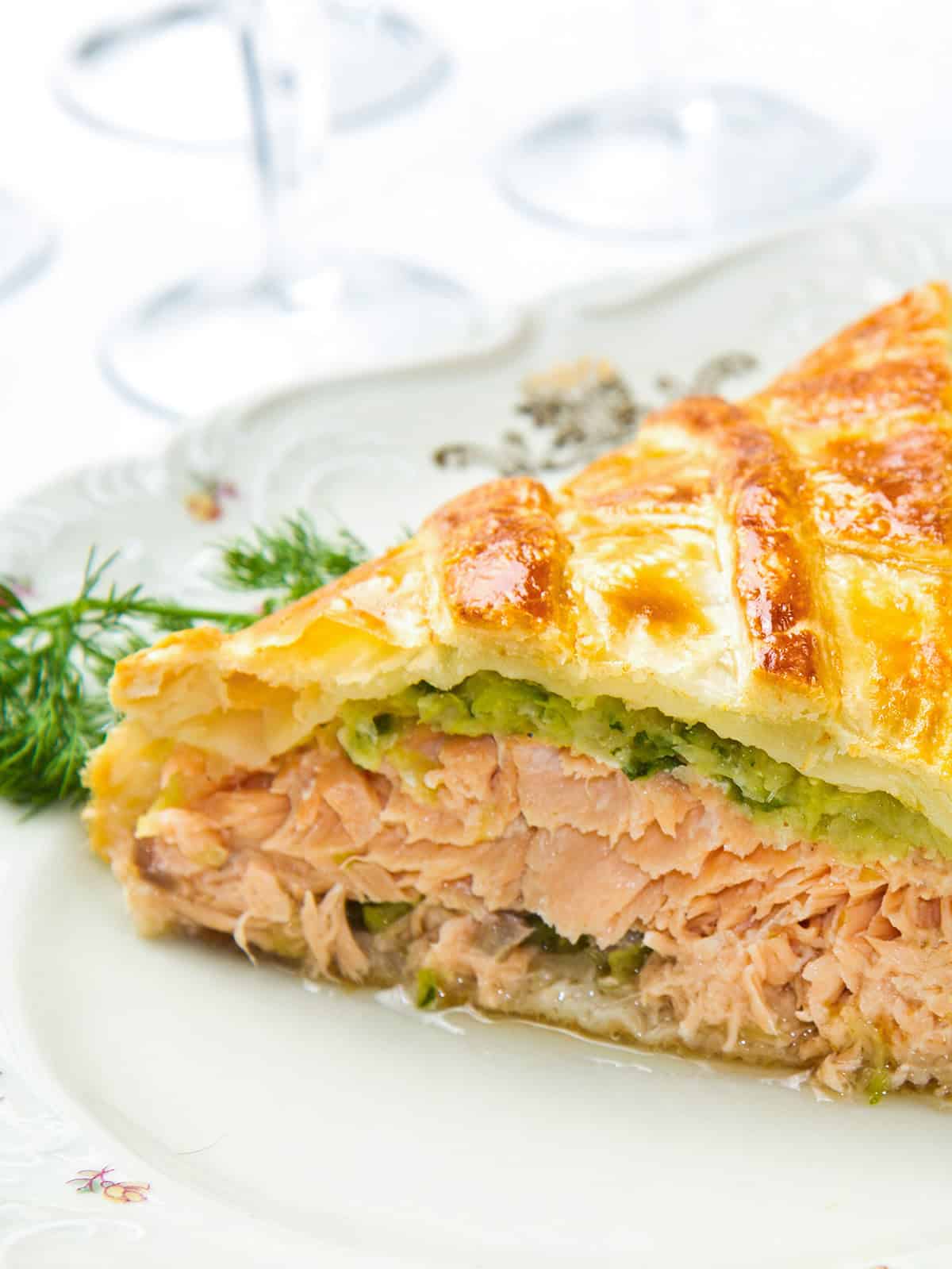 A slice of salmon Wellington, with its golden pastry crust, sits elegantly on a plate, garnished with a small sprig of dill.