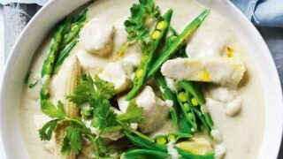 A bowl of green Thai curry with fish, green beans, asparagus, and cilantro—one of our Healthy 5 Ingredient Spring Dinners—garnished with fresh cilantro and a lime half on the side.
