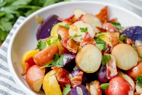 Side view of German Potato Salad in a white bowl with fresh parsley