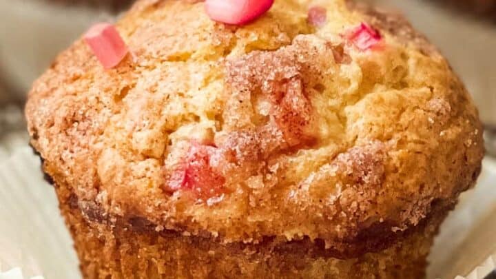 Close-up of several puff pastries topped with a dollop of whipped cream, a small piece of strawberry rhubarb, and a fresh mint leaf on a wooden surface. The image is high-quality and focuses on the fine details of the pastries' texture and toppings.