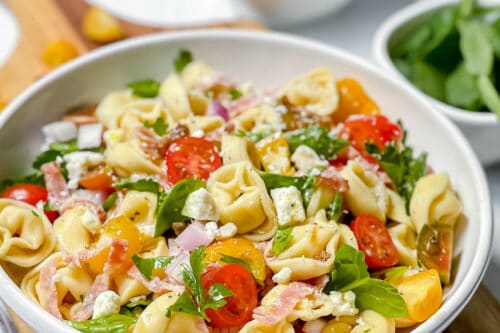 Side view of Tuscan Tortellini Salad in a white bowl with fresh spinach and feta