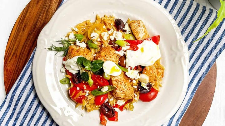 Top view of Greek Chicken and Orzo Skillet on a scalloped plate with fresh herbs and cherry tomatoes