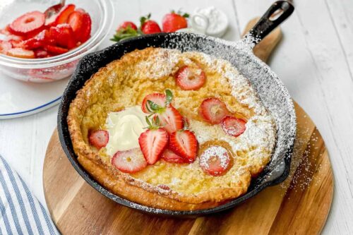 Side view of Strawberry Dutch Baby in a cast iron skillet with fresh strawberries