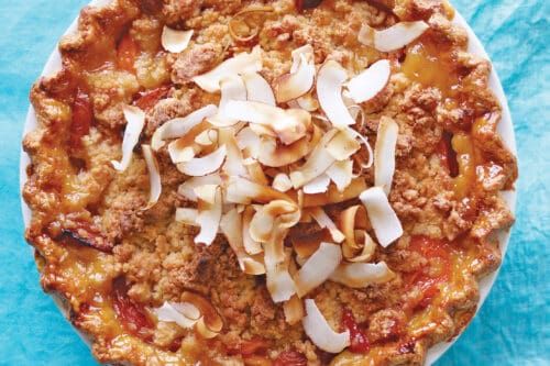 A baked pie with a golden crumb topping and toasted coconut flakes, perfect for picnic desserts, placed on a blue cloth background.