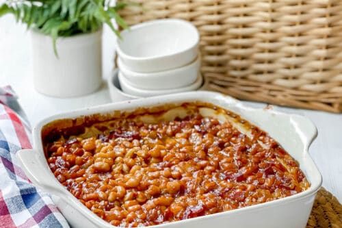 Long view of Boston Baked Beans in casserole dish with picnic basket in the background