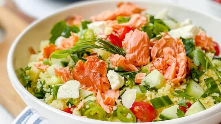 Side view of Mediterranean Couscous Salad with flaked smoked salmon in a white salad bowl