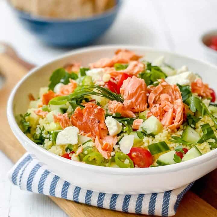 Side view of Mediterranean Couscous Salad with flaked smoked salmon in a white salad bowl