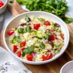 Greek Orzo pasta salad with fresh parsley, vegetables and Mediterranean olives with more fresh herbs on the side.