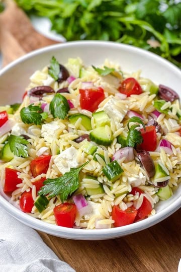 Greek Orzo pasta salad with fresh parsley, vegetables and Mediterranean olives with more fresh herbs on the side.