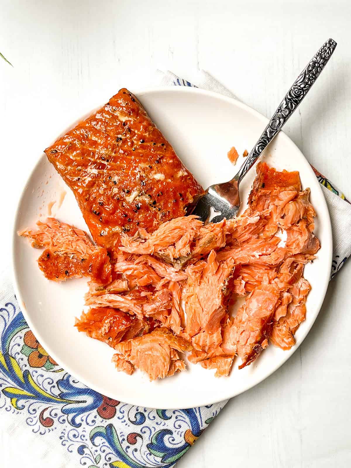 A plate with a smoked salmon, partially flaked with a fork resting on the plate. 