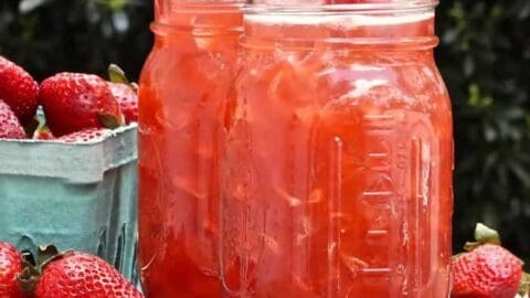 A jar of red liquid next to strawberries, perfect for drizzling over your favorite 20 Minute Skillet Dinners.