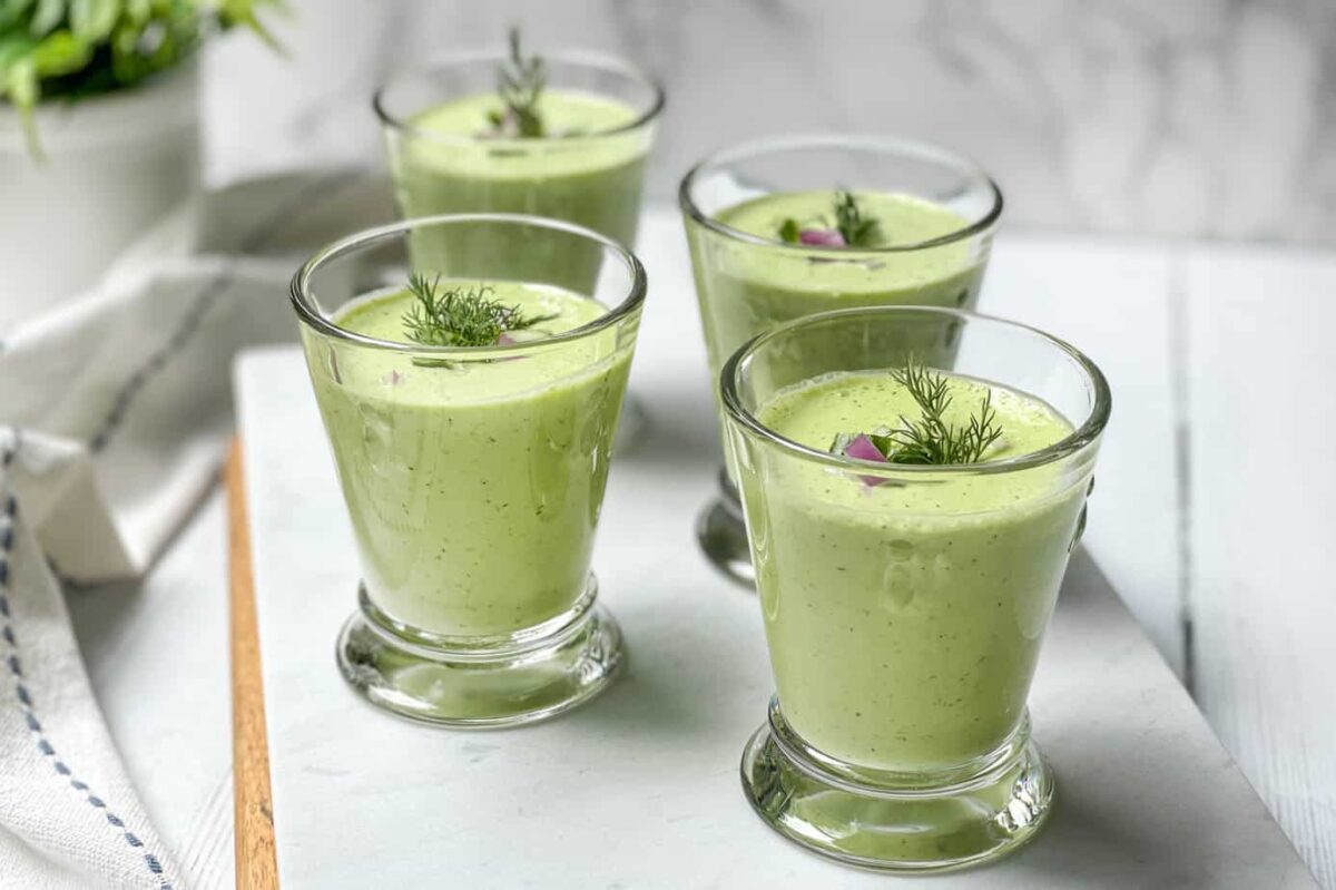 Side view of glasses of cucumber soup garnished with dill and red onion