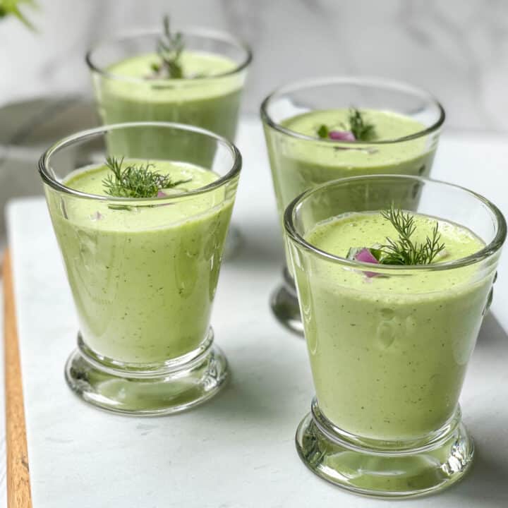 Side view of glasses of cucumber soup garnished with dill and red onion