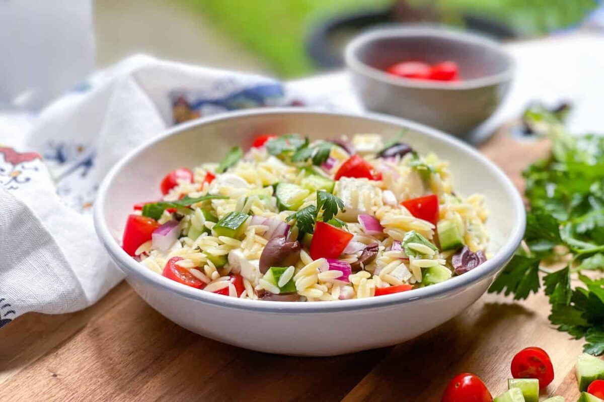 Side view of Greek Orzo Salad in a white bowl with cherry tomatoes