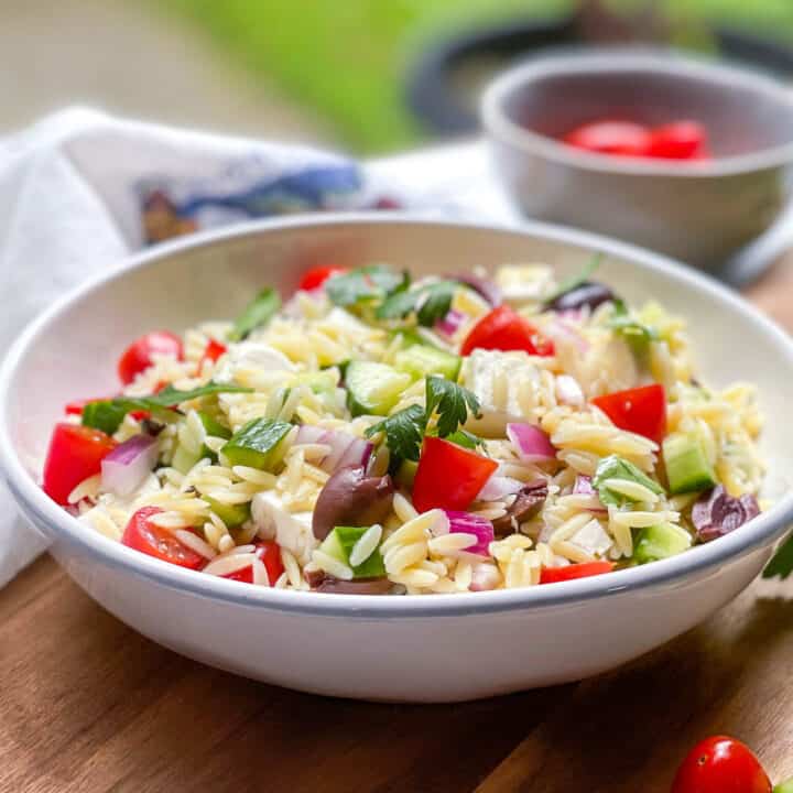 Side view of Greek Orzo Salad in a white bowl with cherry tomatoes