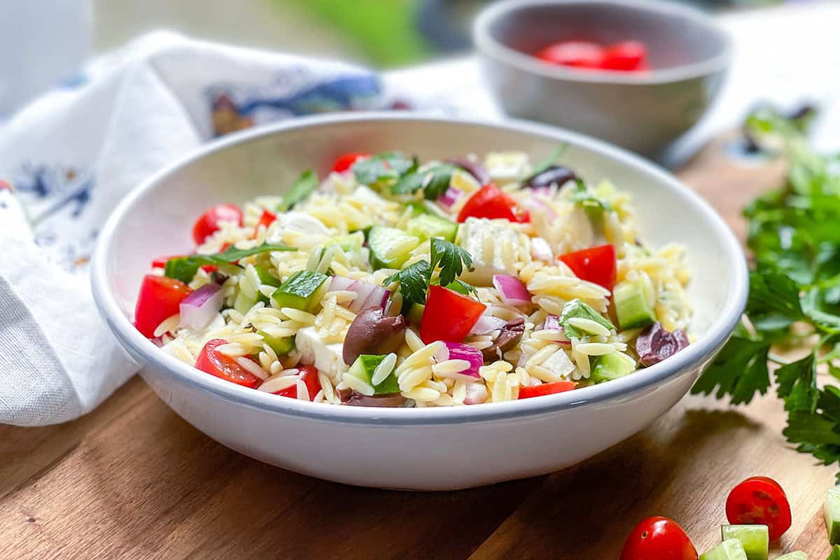 Bowl filled with Greek Orzo Pasta Salad with Mediterranean olives, cucumbers, and peppers for a delicious pasta salad.