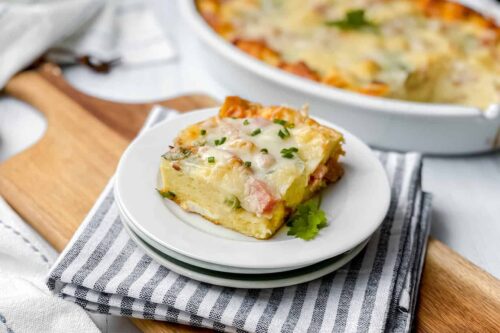 Serving of Ham and Cheese Strata on a white plate with fresh chives and parsley