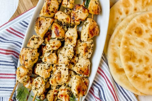 Top view of skewers of souvlaki with fresh dill on a white platter