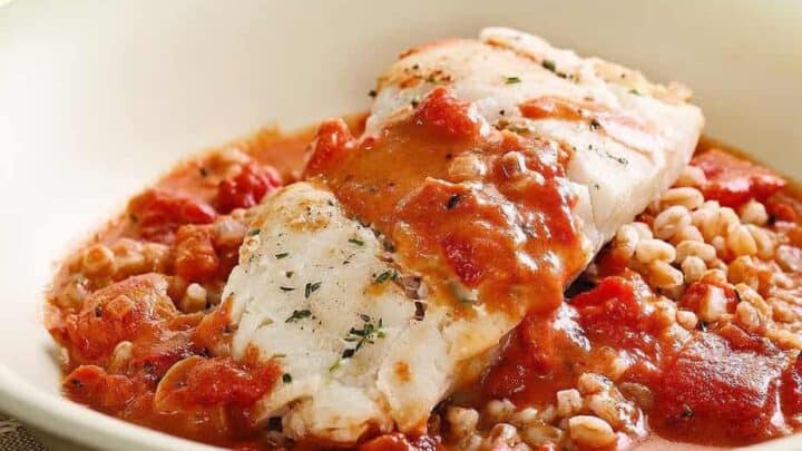 A white fish fillet served on a bed of grains with a chunky tomato-based sauce in a white bowl—an effortless addition to your One Pot Summer Dinners.