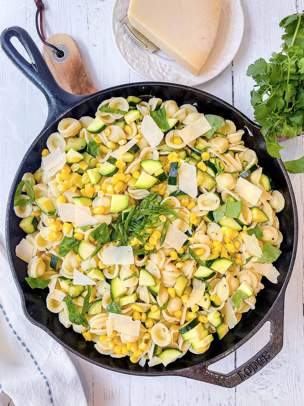 Corn and zucchini pasta in a large cast iron skillet topped with fresh herbs and Parmesan shavings.
